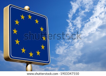 Closeup of a modern road sign with the European Union Flag on blue sky with clouds and copy space.
