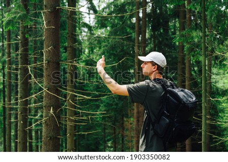 A young man catches a cellular network on a smartphone while walking in the mountains, stands in a beautiful coniferous forest and uses a smartphone.