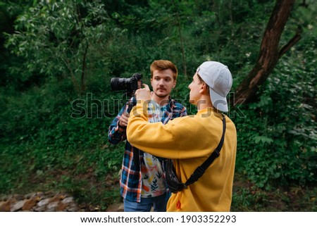 Two male video makers create videos in nature, a guy holds a camera on a stabilizer and communicates with a colleague. Friends shoot travel videos on vacation on a hike. Creating video content.