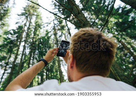 Man shoots trees and sky in the forest on a smartphone camera on a hike. Guy makes photo content in the mountain forest for social networks.