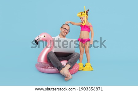 Young businessman freelancer with child daughter works remotely on a laptop, sitting on an inflatable ring in the shape of a pink flamingo. Trades cryptocurrency and bitcoin on the stock exchange. 