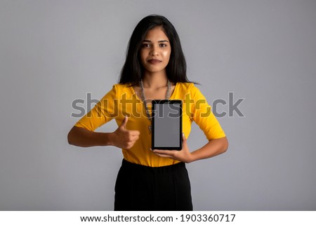 Young beautiful girl holding and showing blank screen of smartphone or mobile or tablet phone on a gray background.