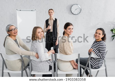 happy interracial businesswomen and cheerful speaker smiling during lecture
