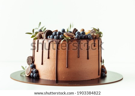 Chocolate cake decorated with blueberries, cookies and chocolates on a white background. Flat lay of the brown birthday cake Royalty-Free Stock Photo #1903384822