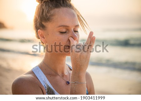Woman's face close up. Yogi woman practicing Nadi Shodhana Pranayama, Alternate Nostril Breathing. Breathing exercise. Self care concept. Stress and anxiety relief. Yoga retreat. Thomas beach, Bali Royalty-Free Stock Photo #1903411999