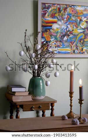 Flowering willow branches in a vase with hanging eggs. Easter bouquet in a vase on a etagere bookcase