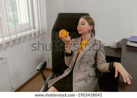 Business lady holding an orange while sitting at the table in her office