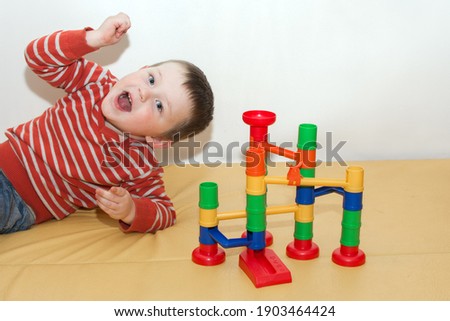 A happy child lies and plays in a maze with a rolling ball. An educational game for a child. Multi-colored toy for the development of logical thinking, observation. Horizontal photo
