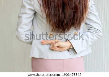 businesswoman with fingers crossed behind her back. Trickery Concept.Business partners shaking hands with one of them holding fingers crossed behind back.