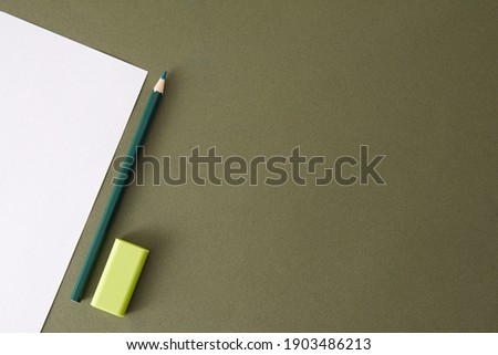 Green pencil, white paper and eraser. Empty place for text or drawing on the green background.
