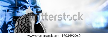 Mechanic holding tire with copy space for text repair service center, blurred background, Maintenance transport  panorama or banner photo. Royalty-Free Stock Photo #1903492060