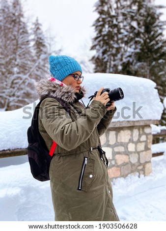 Nature woman landscape photographer in warm clothing  taking picture photos with DSLR camera on Kranjska Gora, Slovenia. Winter activities. Winter holidays. 