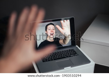 A young woman in a laptop's screen waving and smiling. Online video chat with friends waving to each other Royalty-Free Stock Photo #1903510294