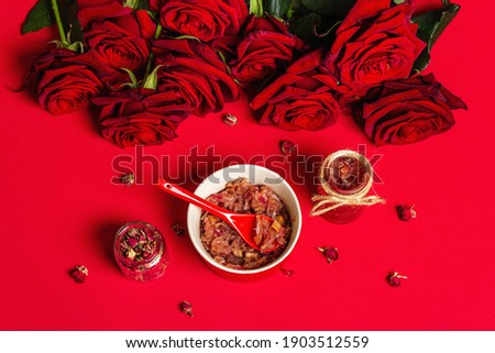 Homemade rose petals jam. Sweet breakfast for lovers, bouquet of fresh roses, festive decor. Valentines Day, Wedding or Birthday concept, matte red background