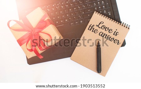 Valentine's day concept. Creaft gift box with red ribbon,laptop,black marker and craft colour notepad with LOVE IN THE ANSWERS sign