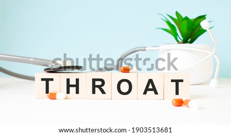 The word THROAT is written on wooden cubes near a stethoscope on a wooden background. Medical concept