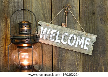 Wood welcome sign hanging on wooden background by glowing antique lantern