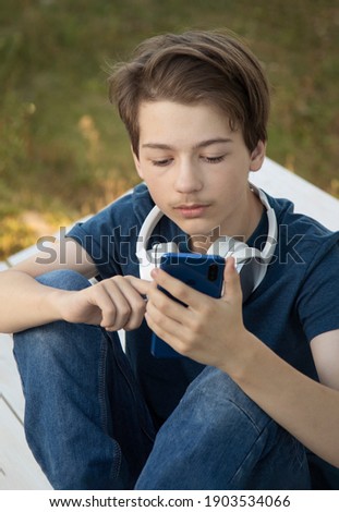 Teenager Holded in Hand Smartphone . Boy look in cell phone and take picture on summer background