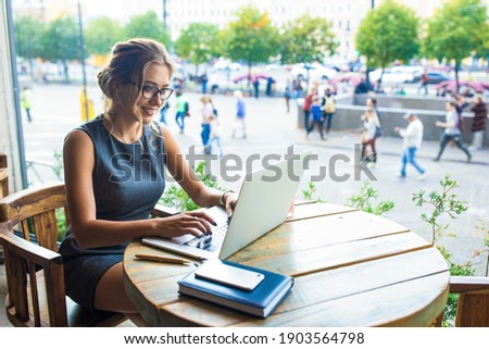 Smiling joyful woman in glasses smart government worker online working on laptop computer while sitting in restaurant during coffee break. Female student checking email via notebook 