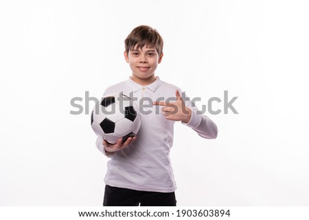 A nice picture of a boy holding a soccer ball and smiling at the camera is pointing at it .
