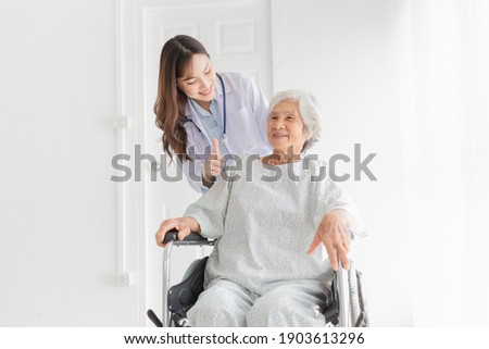 close up patient, Asian doctor drive a wheelchair and show thumb up sign with hand, doctor and old female talk about symptoms and treatment plan, rehabilitation activity, elderly healthcare promotion Royalty-Free Stock Photo #1903613296