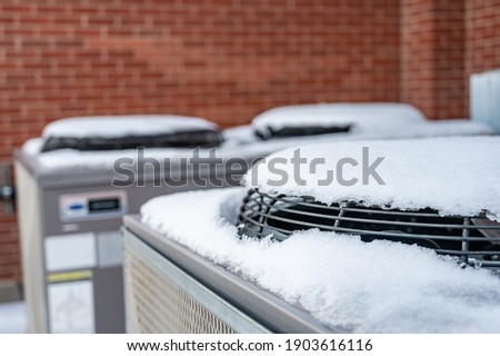 Outdoor mechanical air conditioning units idling during the winter with snow on top of the fans Royalty-Free Stock Photo #1903616116