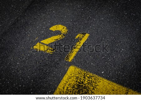 Grey asphalt road, yellow painted number twenty one on grey street, yellow lines like a corner on the road, space for text 
