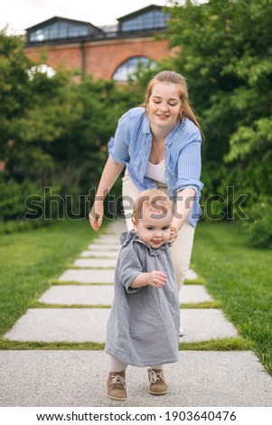 A young mother walks with a one-year-old baby, holds him in her arms, hugs. Communication with the child for his harmonious development
