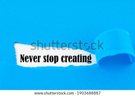 Text Never stop creating appearing behind torn blue paper