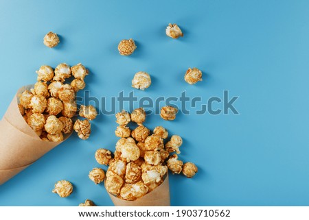 Popcorn in caramel glaze in a paper envelope on a blue background. Delicious praise for watching movie movies, serial, cartoon. Free space, top view. Minimalistic concept.