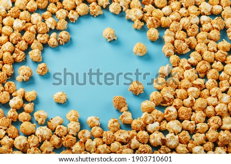 Caramel popcorn by a ripple on a blue background, in the form of a frame. Delicious catch for the films of movies, serials, cartoons. Free rightful, crimes. Minimalistic concession.