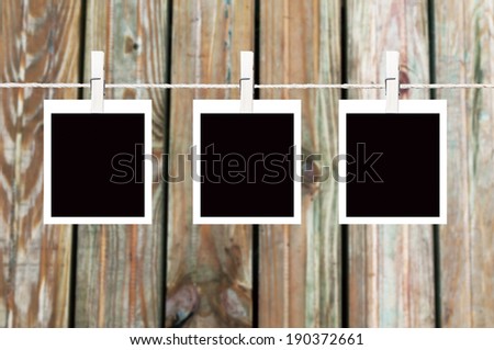 Three blank instant photos hanging on the clothesline. On old wooden background.