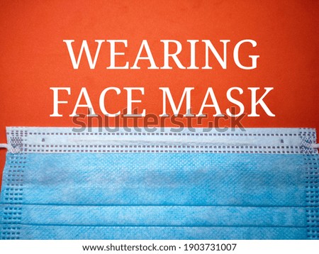 Selective focus of a face mask and word WEARING FACE MASK on a red background.Shot were noise and film grain.