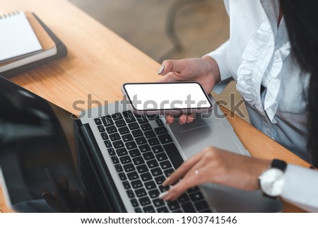 Business woman using mobile phone and laptop on the desk in the office. Blank white screen. Mock up.