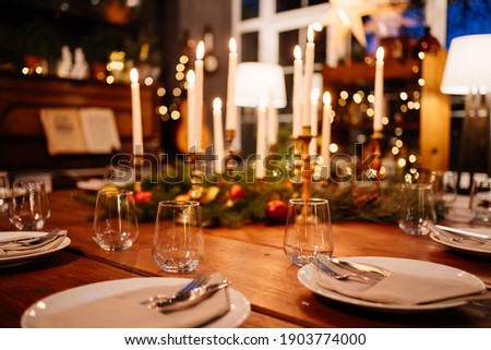 A large square wooden table served for Christmas dinner in a country house with large windows. Evening shooting. new year with friends and family. The interior is retro styled. Low light.
