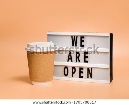 Disposable beverage cup and lightbox with the words "We are open" on a pastel background with copy space.