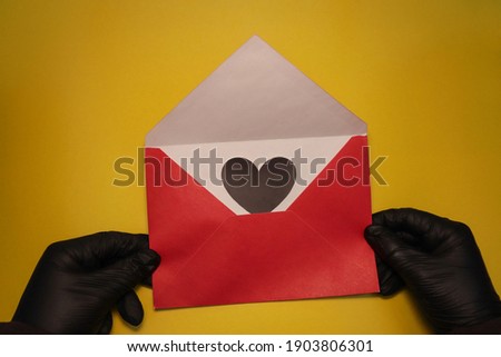 Love letter. Red envelope with a heart. Heart in an envelope.  Envelope in hands. Black gloves. The concept of support, love, care and gratitude to doctors and healthcare workers.