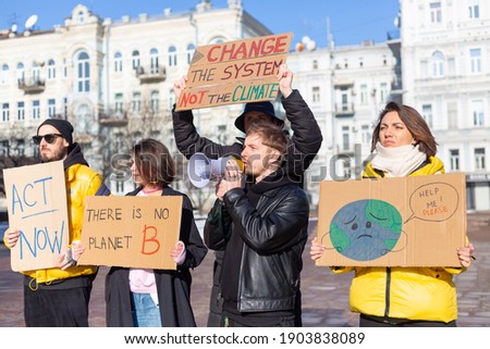 A group of people with banners and a megaphone in hand are protesting in the city square for svae planet clean world act now