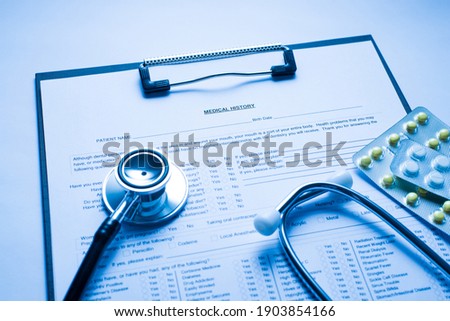 Close up photo image of clipboard with medical history stethoscope ans pills in blisters on doctor's workplace