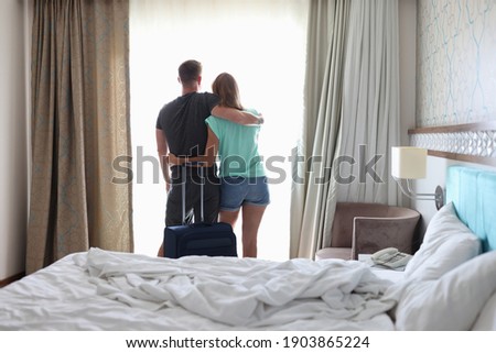 Man and woman are hugging each other near window next to suitcase. Where to go on romantic trip concept