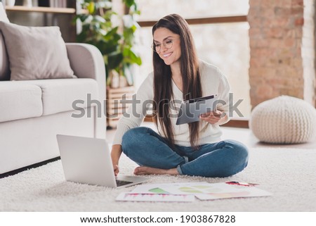 Photo of woman sit carpet hold e-book look pc screen toothy smile wear eyewear white pullover in living room home indoors