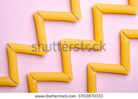 Italian pasta, raw penne tube macaroni zigzag pattern on pink background, top view, abstract food