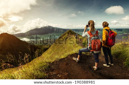 Two hikers with backpacks standing on top of the mountain enjoying valley view and taking a pictures