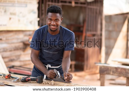 young african carpenter smiling while working Royalty-Free Stock Photo #1903900408