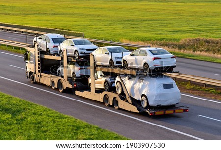 Car carrier trailer transports cars on highway on sunset background. Auto transport and car shipping services concept. Truck with Semi-remorque. Cars Shipping. Car transportation Royalty-Free Stock Photo #1903907530