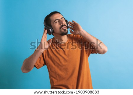 Young handsome man dancing and singing songs listening to music in headphones on a blue background. Happy male enjoying music.