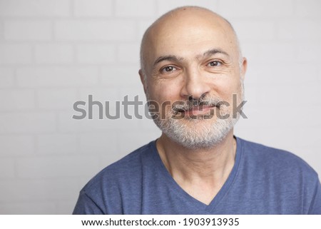 Portrait of a handsome 50 years old man with unshaven hair in a blue t-shirt indoors. Royalty-Free Stock Photo #1903913935