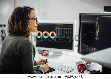 Profile view of Female graphic designer at the office with two displays, editing photos and video with a pen tablet. Business woman working concentrated. Freelance worker at Creative office studio.