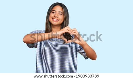 Young latin girl wearing casual clothes smiling in love doing heart symbol shape with hands. romantic concept. 