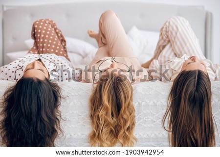 On a bed. Picture of three long-haired girls lying on bed
